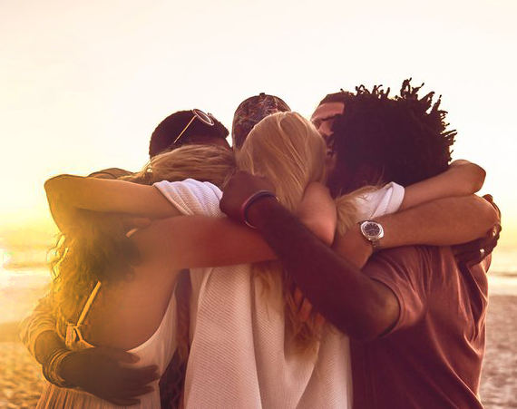 A group of people hugging with the sun setting behind